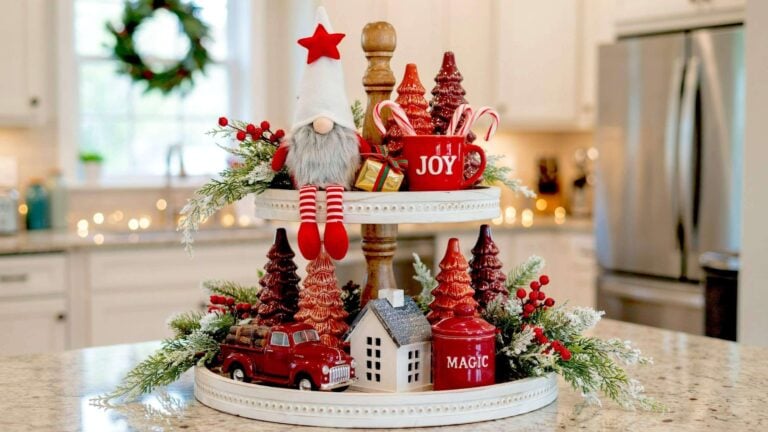 Rustic wooden two-tier stand holding a plush Christmas gnome beside red ceramic trees, a vintage toy truck, and frosted greenery for Christmas tiered tray ideas.