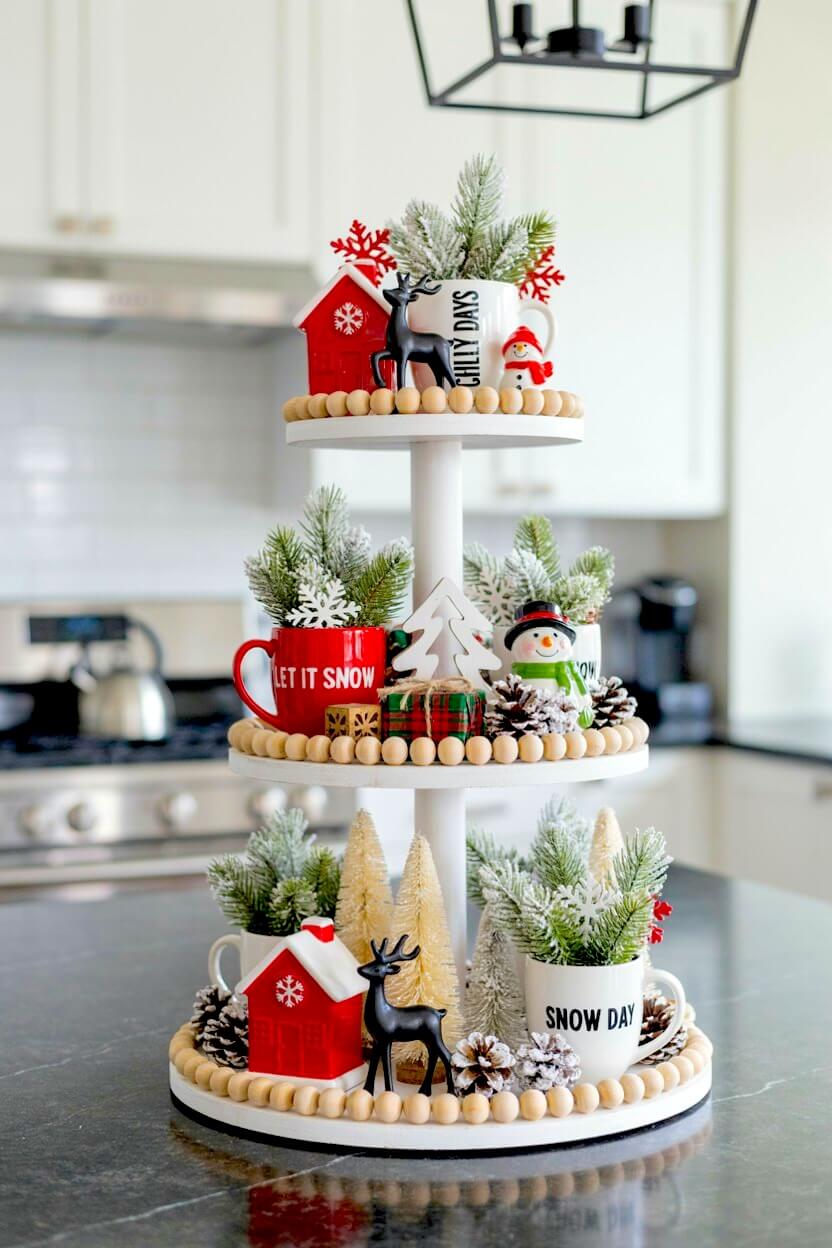 White wooden stand decorated with bright red mugs holding frosted pine, snowy miniature ceramic houses, and small black reindeer figures for seasonal tray design.