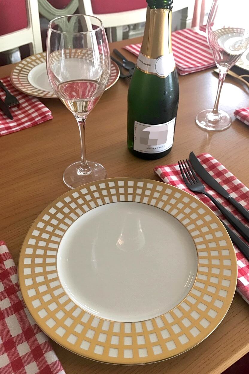 A gold-accented dinner plate set against red gingham napkins and sparkling wine glasses creates a casual yet festive setup for Thanksgiving table setting ideas.