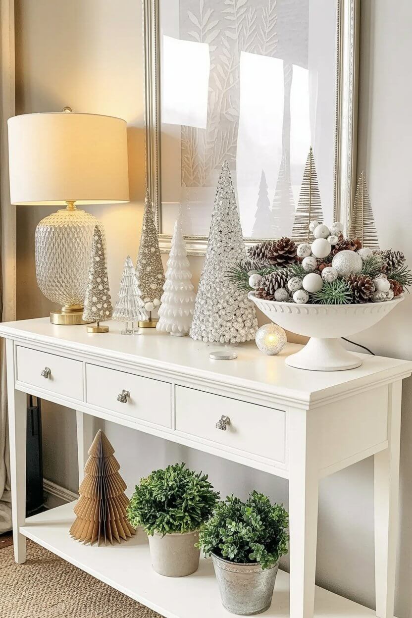 A bright white console table displays an assortment of shimmering trees, snowy pinecones, and a full winter bowl arrangement. Soft gold lighting and clean styling make these white Christmas decor ideas feel modern and serene.