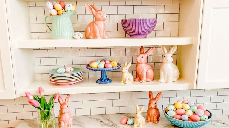 Wide shot of white kitchen shelving decorated with pastel ceramic bunnies speckled eggs and pink tulips for easter kitchen decor ideas.