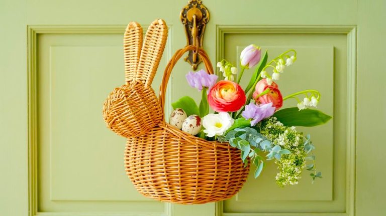 Wicker bunny basket hanging on a sage green door filled with red ranunculus, purple tulips, and speckled eggs for charming front door basket ideas.