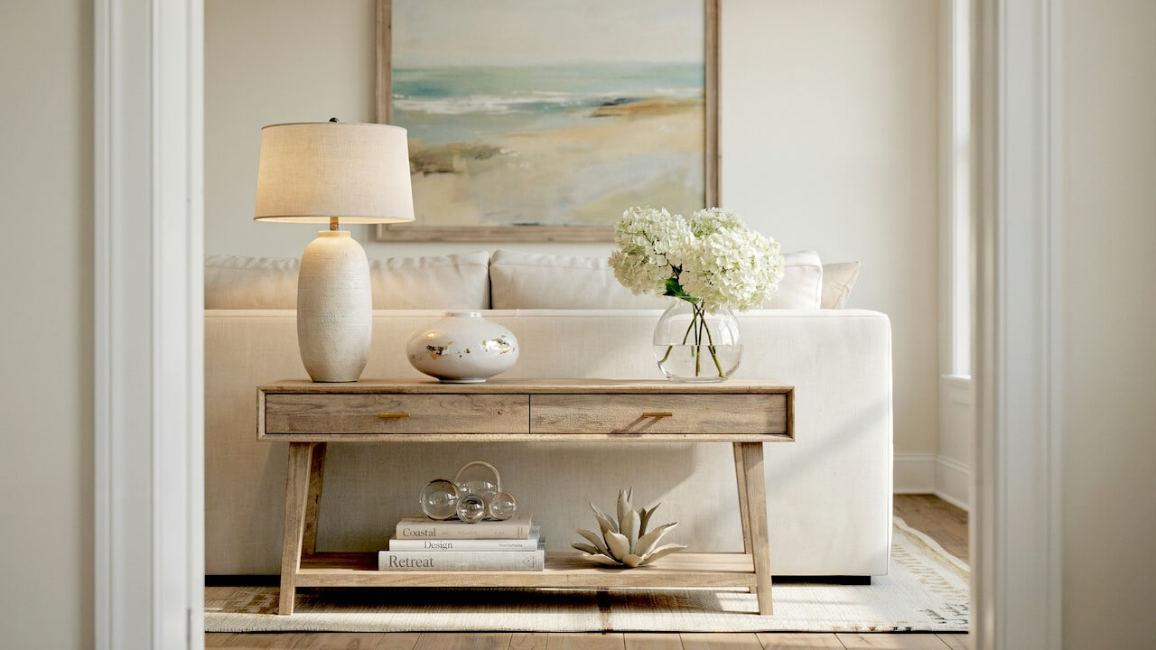 A light wood table behind a sofa showcases small console table decor ideas, styled with white hydrangeas, a textured ceramic lamp, and a coastal painting.