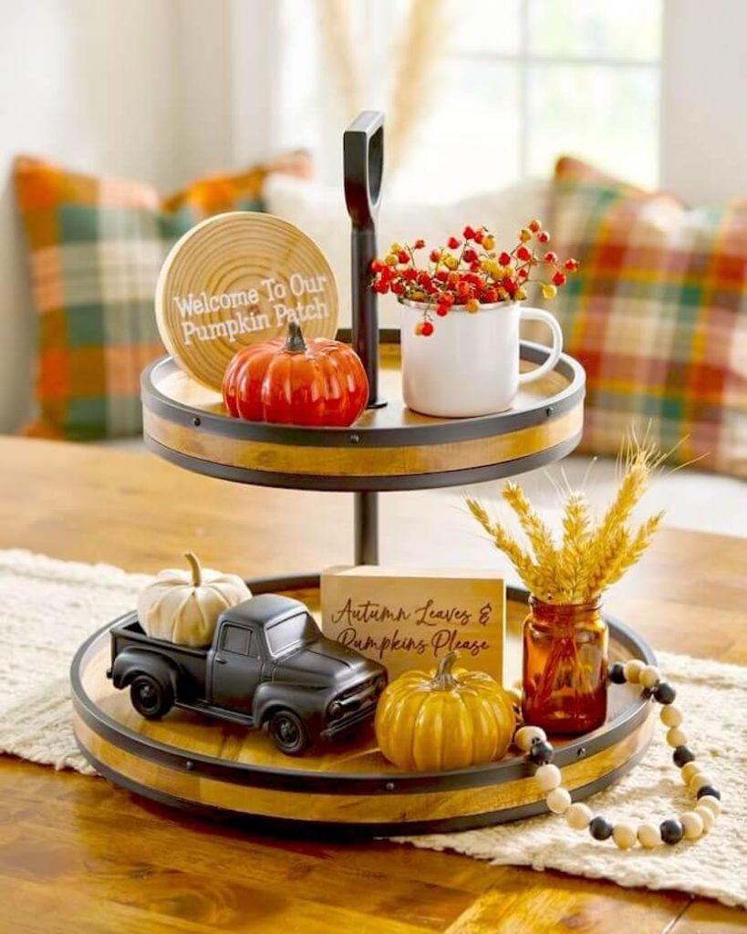 A matte black decorative truck, a glossy orange pumpkin, a white enamel mug with red berries, and wheat stems styled as a rustic fall counter arrangement.