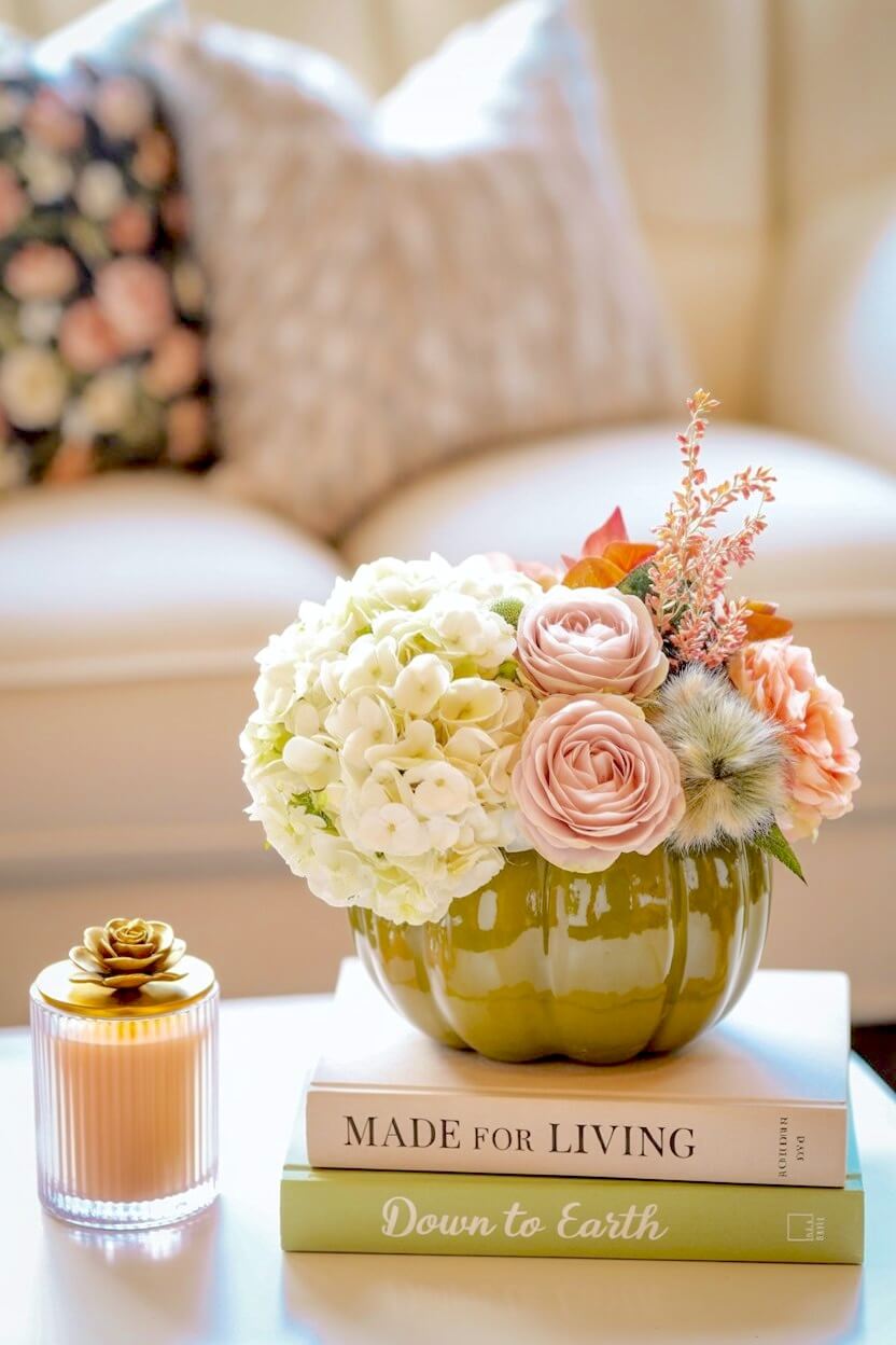 Olive green glazed ceramic pumpkin flower vase holding white hydrangeas, dusty pink roses, and fluffy green trick dianthus resting on stacked decor books.
